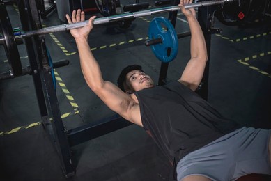 a fit asian man in his late 20s doing flat barbell bench presses. working out chest at the gym. compound exercise program.