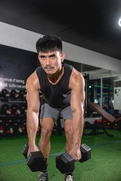 a fit asian man does bent-over dumbbell rows. weight and resistance training at the gym.