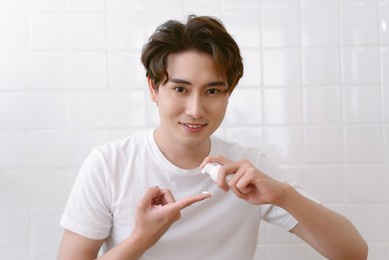 portrait of young asian man with squeezing cream on his hand do morning self-hygiene routine apply skincare cosmetics product, after shave moisturizing lotion and looking at camera. skincare concept