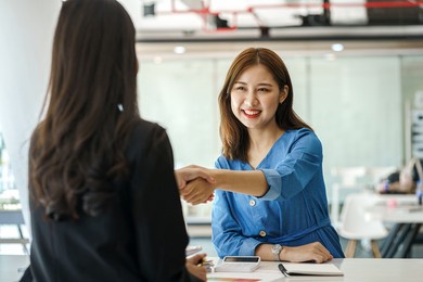 pretty attractive brunette asian business woman shaking hands with friend in modern office during meeting.