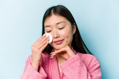 young asian woman holding a facial disk isolated on pink background