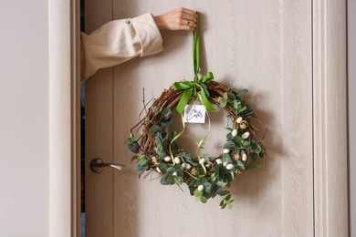 woman hanging easter wreath on wooden door, closeup