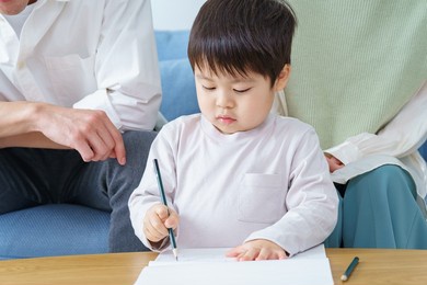 a boy working on drawing with a pencil and his parents watching over it