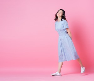 full length image of young asian woman wearing blue dress on pink background