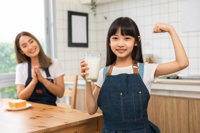 asian  family enjoying breakfast at cozy kitchen, little girl daughter sitting on table, drinking milk with smiling father and mother in morning. happy family in kitchen.