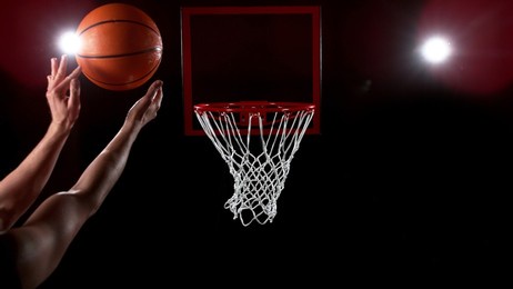 basketball going through the basket on black backgorund, detail shot. man hands silhouette in front of the shot.