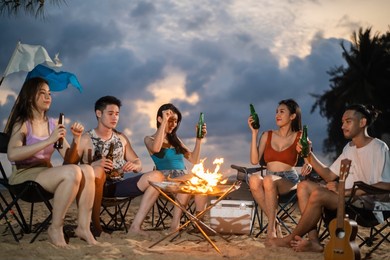 group of asian young man and woman having party on the beach at night. attractive friends traveler sing and dancing while camping at seaside enjoy holiday vacation trip in tropical sea island together