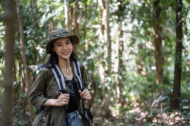 portrait of asian beautiful woman backpacker traveling alone in forest. attractive girl traveler walk in nature wood with happiness and fun during holiday vacation trip then smiling, looking at camera