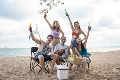 group of asian young man and woman having party on the beach together. attractive happy friends traveler singing and dancing while camping at seaside enjoy holiday vacation trip in tropical sea island