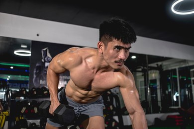 a serious and muscular asian guy training doing one arm dumbbell rows on a bench. shirtless, vascular and ripped. training back muscles.