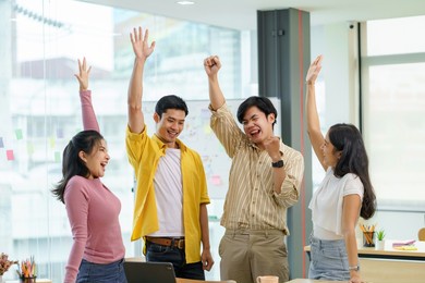 happy group of young asian business people in casual wear successful excited raised hands rejoicing. new startup project concept.