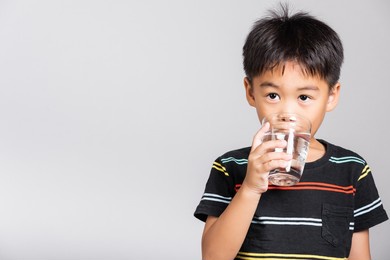 little cute kid boy 5-6 years old smile drinking fresh water from glass in studio shot isolated on white background, asian children preschool, daily life health