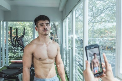 a man recording a fitness vlog with his friends help at the gym. showing off a chiseled physique and giving tips.