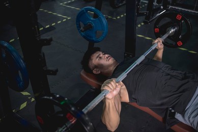 a fit asian man in his late 20s doing flat barbell bench presses with a moderate weight. warmup set for chest exercise. working out upper body at the gym.