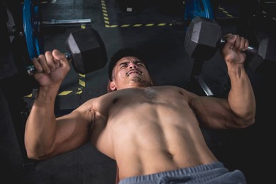 a determined man fights the pain while doing a high rep set of dumbbell bench presses to failure. chest workout at the gym.