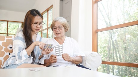 family care concept and the elderly, an asian woman reading a label recommending her mother in taking medicine.