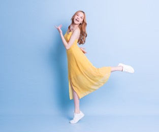full length image of young asian woman wearing yellow dress on blue background