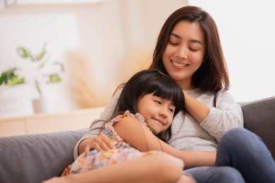 asian mum her little daughter hugging sit on sofa smile.loving family portrait, mothers day celebration concept .