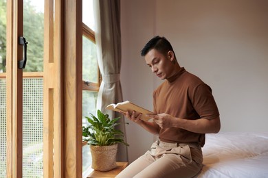 serious young asian man sitting on bed and reading book of stories