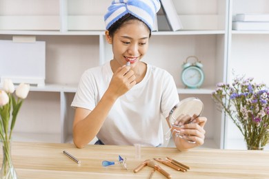 cozy lifestyle concept, young woman in turban after shower and use lipstick for make up at home.
