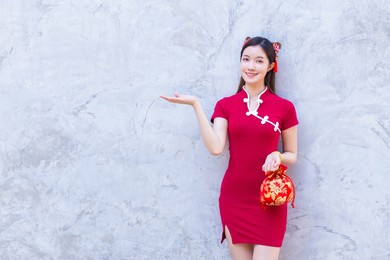 asian beautiful woman in red dress stands holding a red bag among old city center chinese new year theme.