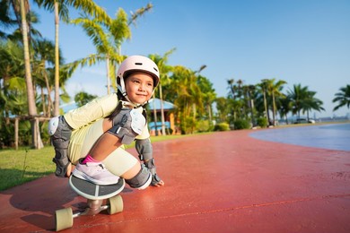 asian child or kid girl playing skateboard or surf skate in skating track and extreme sports exercise by crouching to turn hand touch floor to wearing helmet elbow knee support for body safety protect