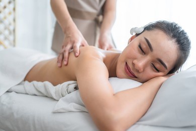 asian young woman feeling happy and relax during back massage with oil. attractive beautiful girl lying on massage table, getting physiotherapy from masseuse for skin and body care in spa beauty salon