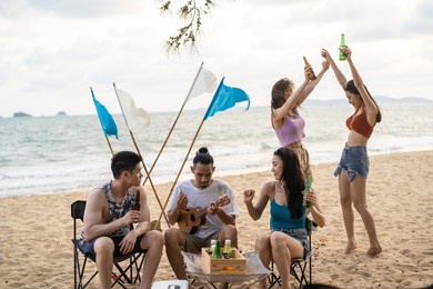 group of asian young man and woman having party on the beach together. attractive happy friends traveler singing and dancing while camping at seaside enjoy holiday vacation trip in tropical sea island