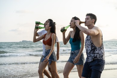 group of asian young man and woman having party on the beach together. attractive friends singing and dancing while walking and running at seaside enjoy holiday vacation trip in tropical sea island.