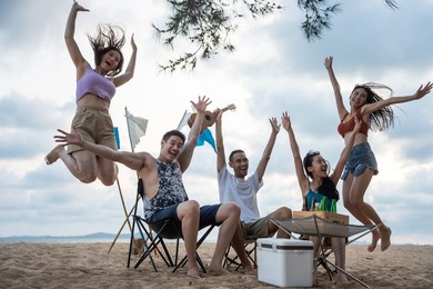 group of asian young man and woman having party on the beach together. attractive happy friends traveler singing and dancing while camping at seaside enjoy holiday vacation trip in tropical sea island