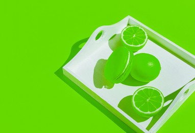 creative composition made of neon green macaroon with lime on white tray on sunlit background. summer refreshment concept.