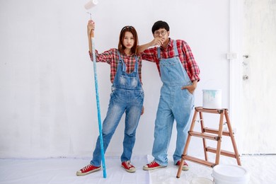 portrait of asian couple in plaid shirt with bear suit painting the interior white wall in new apartment concept,