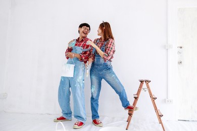 portrait of asian couple in plaid shirt with bear suit painting the interior white wall in new apartment concept,