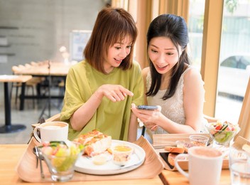  young women sitting in  restaurant looking at mobile phone and smiling