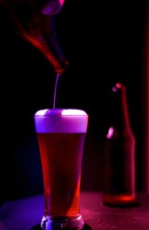 hand pouring beer into glass with blurred bottle on the table in bar, neon light tonig.