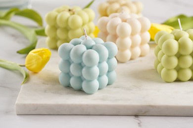 many bubble candles - off-white, beige-colored and blue - on marble board with spring flowers - yellow and purple tulips