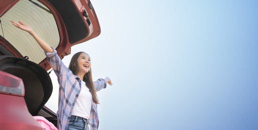 beautiful asian woman is sitting in the 
rear door of sedan.showing arms up smiling happily.cute woman with black hair takes a red saloon.bright sky with free time during the holiday solo travel.