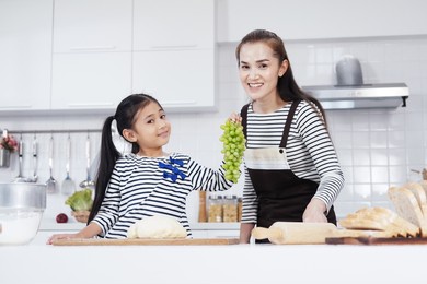 smiling asian mother and little asian girl child funny with grape fruit and baking bakery together in kitchen. homemade pastry for bread. family love and education for homeschool concept.