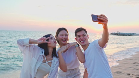 group of happy young adult friends taking selfies on smartphone on a beach at sunset ,group of happy friends spending time together at the beach on summer holidays, friendship, happy summer holidays.