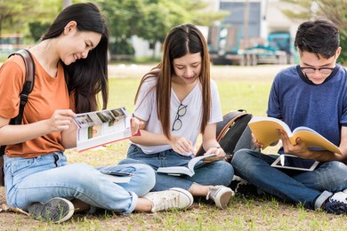 happy young asian young group of man and woman students are sitting during reading books in the park at university, education concept, education back to university concept