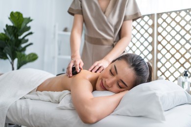 asian young relaxing woman getting back massage therapy with hot stone. attractive beautiful girl lying on massage table, getting physiotherapy from masseuse for skin and body care in spa beauty salon