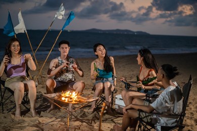 group of asian young man and woman having party on the beach at night. attractive friends traveler sing and dancing while camping at seaside enjoy holiday vacation trip in tropical sea island together