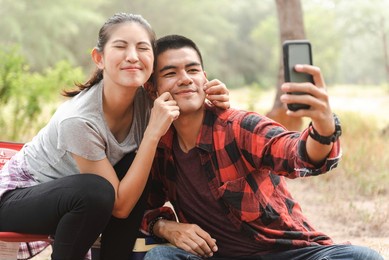 an asian tourist couple takes selfies with their smartphones.