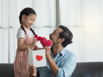 cute girl and handsome asian father putting red hearts together while reading card. father's day or birthday.