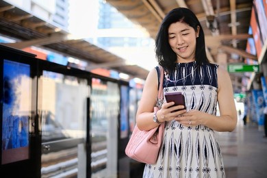 an attractive young confident asian business woman is using her cellphone while waiting for her train at a station to go to work in the morning.  