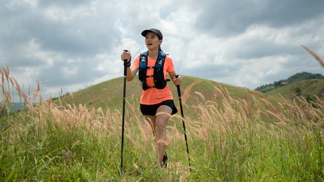 young women active trail running across a meadow on a grassy trail high in the mountains in the afternoon with trekking pole