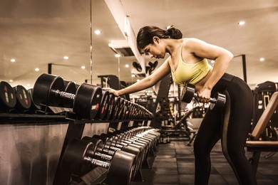 asian bodybuilder woman using dumbbell in fitness gym sport complex. sport, healthy life and lifestyle concept.