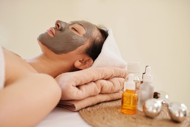 young asian woman relaxing on bed in spa salon with pore clearing clay mask on face