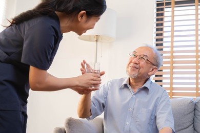 asian young woman caregiver, carer supporting elderly, aged patient at home, drinking water after take medicine, cure or treatment disease of grandmother after retirement, help support.