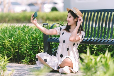 beautiful asian woman wearing hat and dress make a selfie the the park on spring time vacation